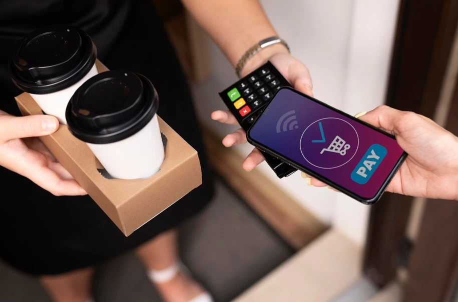 Customer paying with smartphone using mobile POS terminal while holding coffee cups