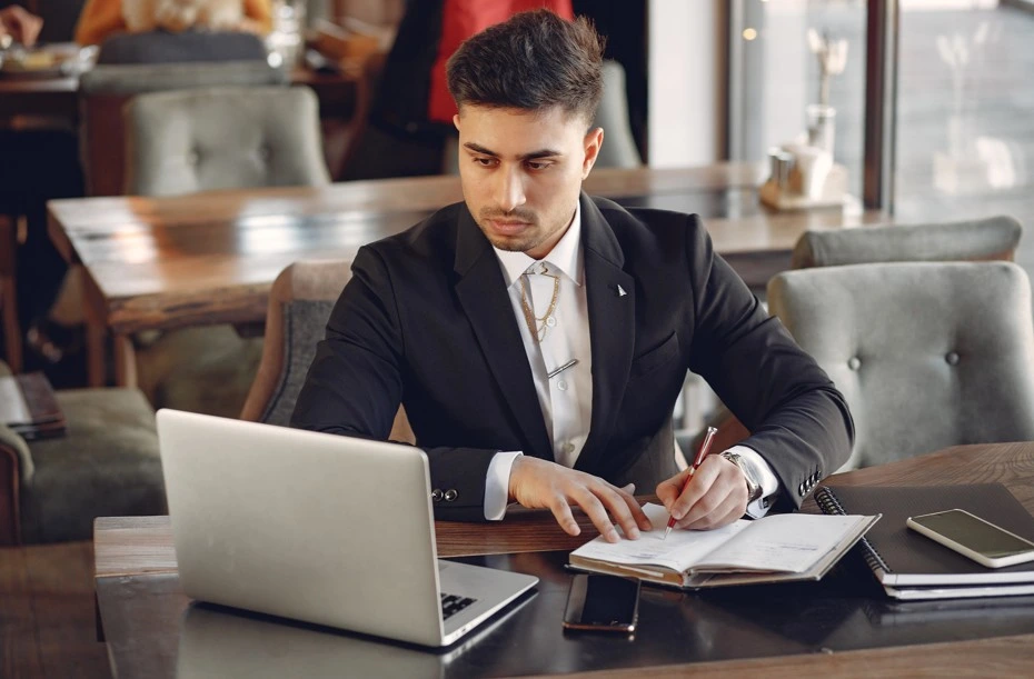 Man working on laptop and taking notes in café