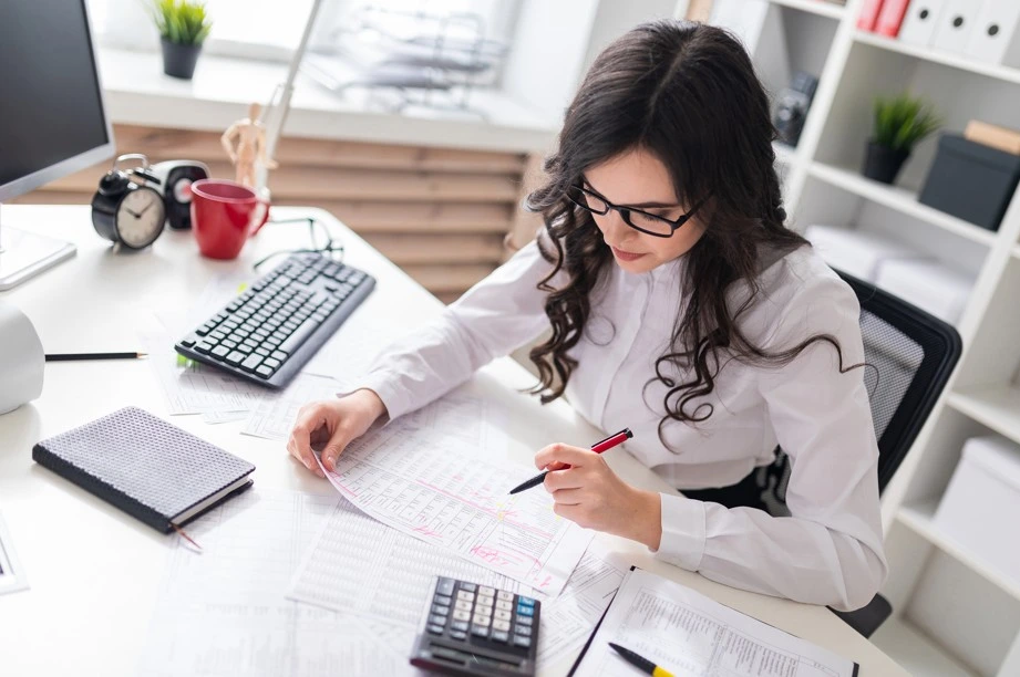 Woman using tablet with calculator and laptop on desk
