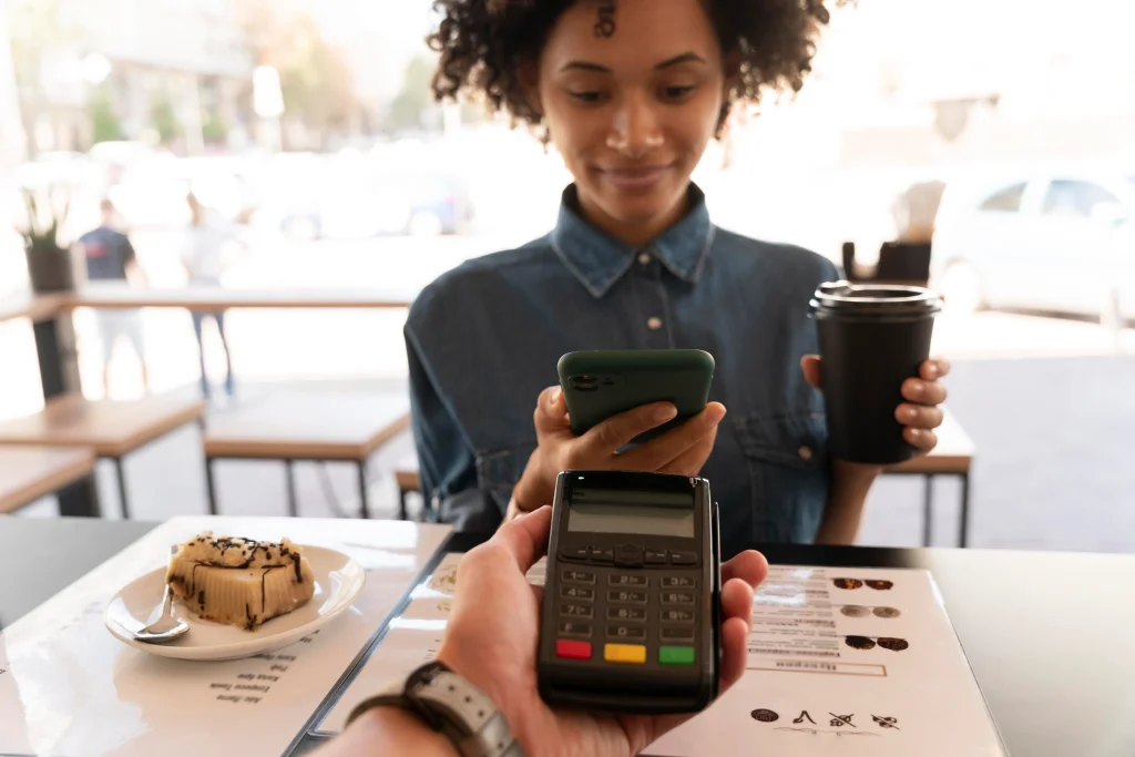 Woman at a café paying with her smartphone using a contactless POS terminal