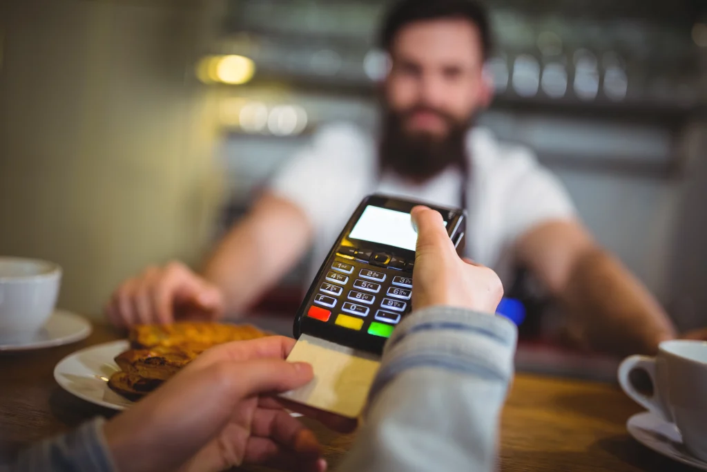 A person in a café holds a card payment machine, ready for a customer. 